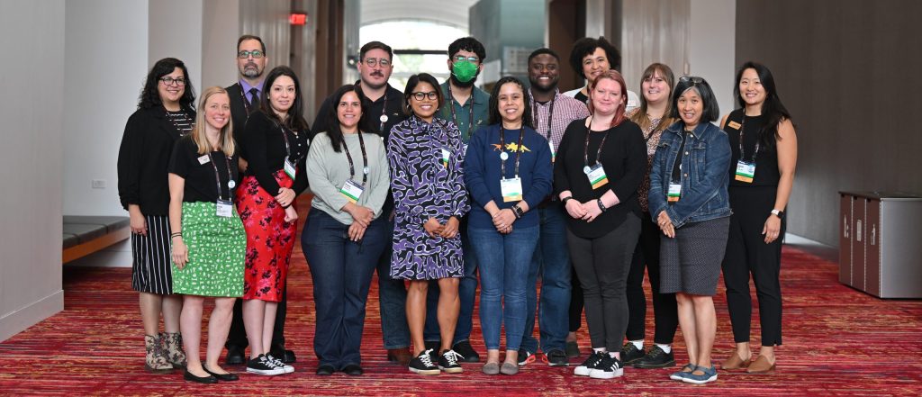 Fifteen individuals pose for a group photo in a conference center hallway.
