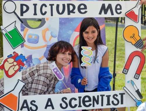 Two girls pose inside an oversized frame that says "Picture me as a scientist"